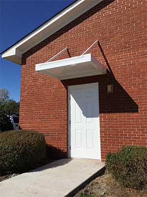 Canopy on a brick wall covering a white door.